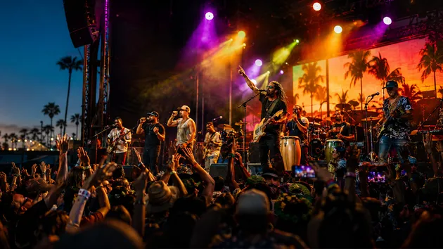 Live reggae band performing for a large festival crowd in San Diego with palm trees and colorful stage lighting